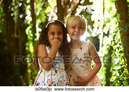 Stock Image - Portrait of two girls wearing tiaras in sunlit forest. Fotosearch