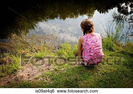 Rear view of girl crouching on riverbank looking water View Large Photo Image Stock Photograph - Rear view of girl crouching on riverbank looking water. Fotosearch
