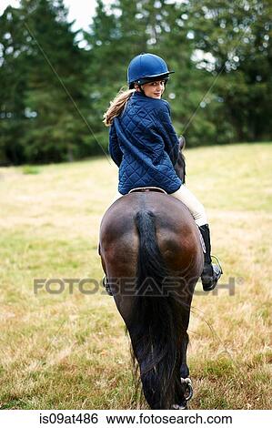 Rear view of girl horseback riding in field View Large Photo Image Stock Photograph - Rear view of girl horseback riding in field. Fotosearch