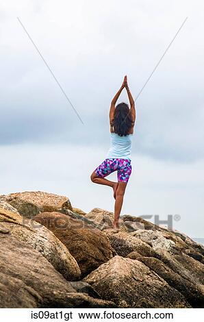 "Rear view of mature woman practicing yoga tree pose on coastal rocks, Cape Cod, USA" View Large Photo Image Stock Photograph - "Rear view of mature woman practicing yoga tree pose on coastal rocks, Cape Cod, USA". Fotosearch