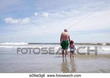 Rear view of senior man paddling in sea with granddaughter View Large Photo Image Stock Photograph - Rear view of senior man paddling in sea with granddaughter. Fotosearch