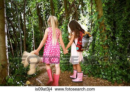 Rear view of two girls carrying teddy bear and backpack walking in forest View Large Photo Image Picture - Rear view of two girls carrying teddy bear and backpack walking in forest. Fotosearch