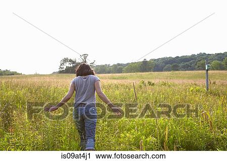 Stock Image - Rear view of woman strolling in field of long grass. Fotosearch