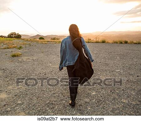 Rear view of young woman carrying guitar case at sunset View Large Photo Image Stock Photo - Rear view of young woman carrying guitar case at sunset. Fotosearch