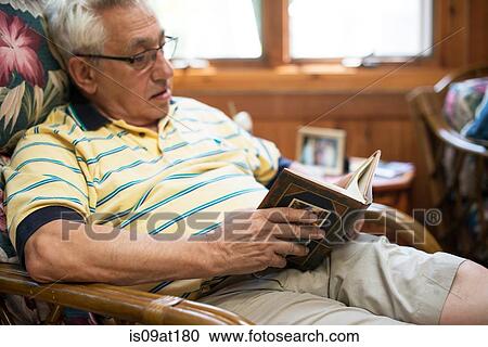 Stock Image - "Senior man, sitting at home, reading book". Fotosearch