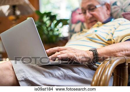Picture - "Senior man, sitting at home, using laptop". Fotosearch