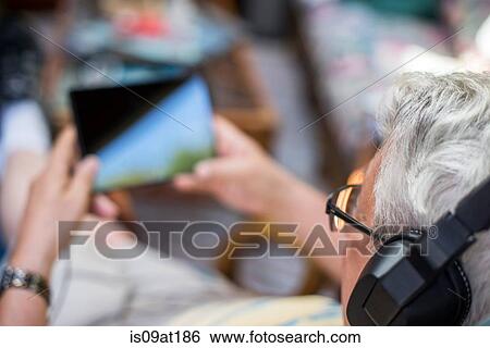 "Senior man, sitting at home, wearing headphones, using digital tablet, elevated view" View Large Photo Image Stock Photograph - "Senior man, sitting at home, wearing headphones, using digital tablet, elevated view". Fotosearch