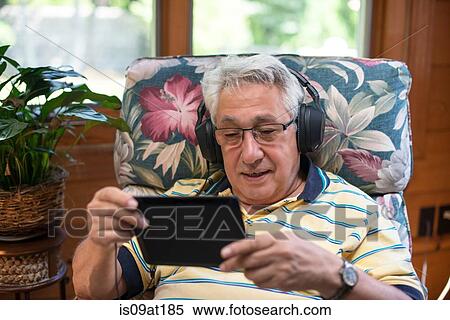 "Senior man, sitting at home, wearing headphones, using digital tablet" View Large Photo Image Stock Photography - "Senior man, sitting at home, wearing headphones, using digital tablet". Fotosearch