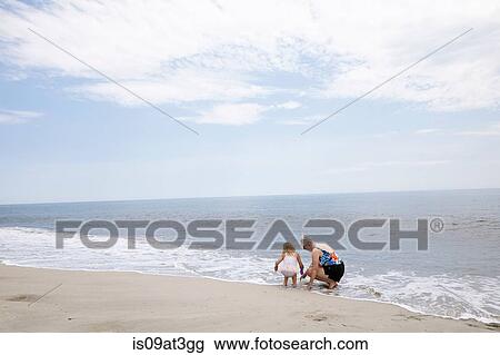 Stock Image - Senior woman and granddaughter crouching and playing in sea. Fotosearch