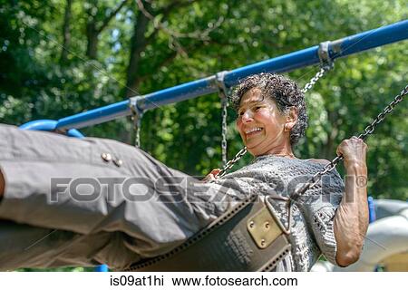 Stock Image - Senior woman in playing on park swing. Fotosearch
