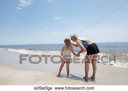 Stock Image - Senior woman pointing for granddaughter on beach. Fotosearch