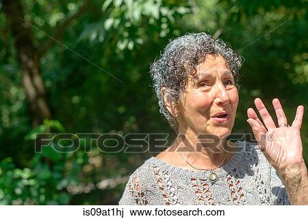 Stock Image - Senior woman waving in park. Fotosearch