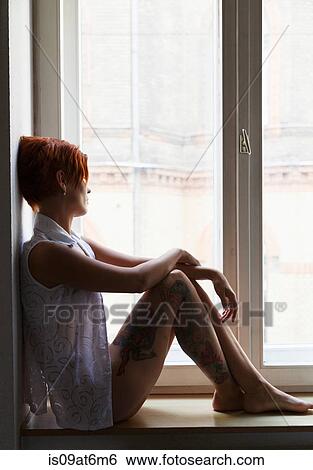 Stock Photograph - Side view of tattooed mid adult woman in window seat looking out of window. Fotosearch