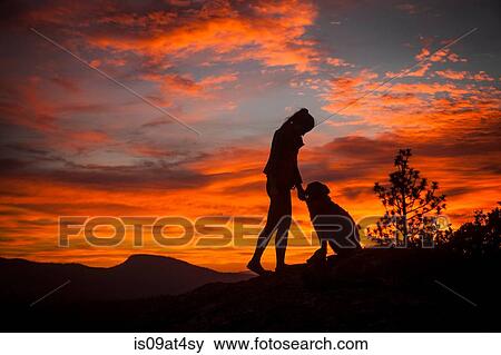 Stock Photo - "Silhouette of young woman and dog with dramatic orange sky, High Sierra National Park, California, USA". Fotosearch