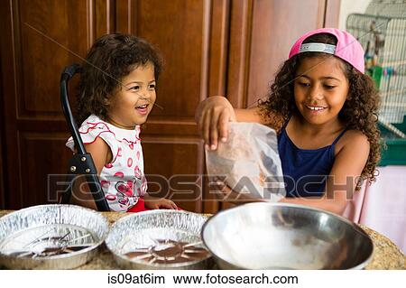 Sisters pouring dried cake mix into mixing bowl smiling View Large Photo Image Picture - Sisters pouring dried cake mix into mixing bowl smiling. Fotosearch