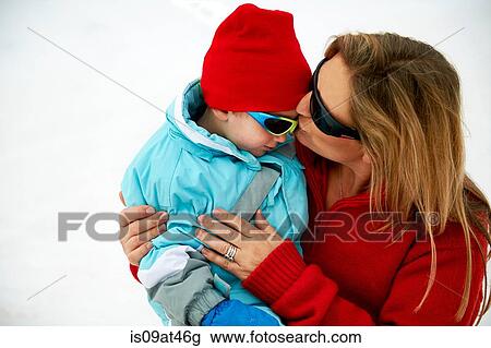 Stock Image - Skiing mother kissing toddler son on forehead. Fotosearch