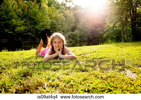 Surface level view of girl lying on front on grass looking at camera View Large Photo Image Picture - Surface level view of girl lying on front on grass looking at camera. Fotosearch