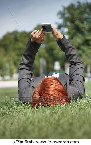Surface view of mid adult red haired woman lying on grass using smartphone View Large Photo Image Stock Image - Surface view of mid adult red haired woman lying on grass using smartphone. Fotosearch