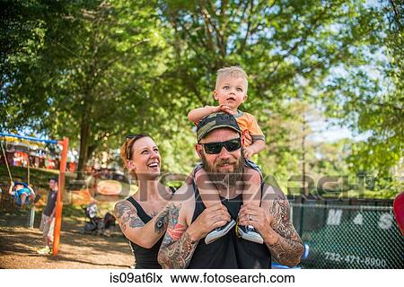 Tattooed father carrying baby boy on shoulders looking at camera smiling View Large Photo Image Stock Photo - Tattooed father carrying baby boy on shoulders looking at camera smiling. Fotosearch
