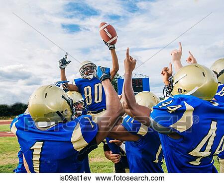 Stock Photo - Teenage and young male American football team celebrating victory on soccer pitch. Fotosearch