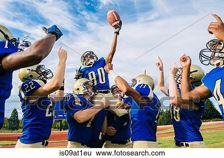 Stock Photograph - Teenage and young male American football team celebrating together on soccer pitch. Fotosearch
