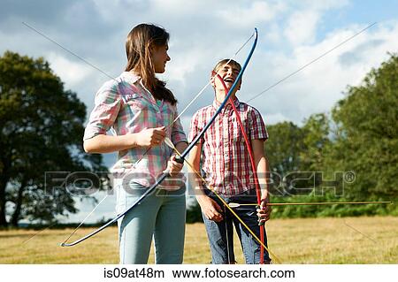 Picture - Teenage girl laughing with teenage brother whilst practicing archery. Fotosearch