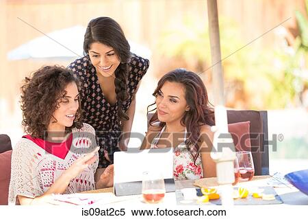 Stock Photography - Three adult sisters browsing digital tablet on patio. Fotosearch