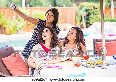 Stock Photo - Three adult sisters taking self portrait on patio. Fotosearch
