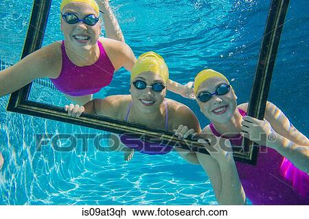 Stock Image - "Three female swimmers, underwater, looking through frame". Fotosearch
