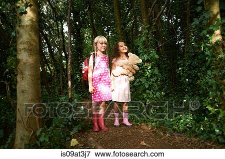 Stock Photo - Two girls carrying teddy bear and backpack in forest. Fotosearch