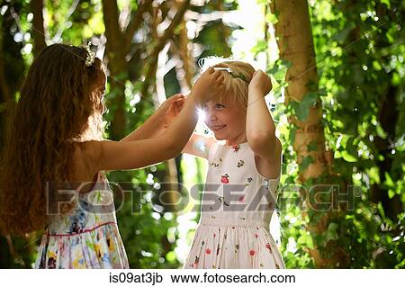 Stock Image - Two girls putting on tiaras in sunlit forest. Fotosearch