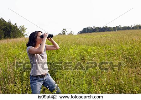 Stock Image - Woman looking through binocculars from field of long grass. Fotosearch