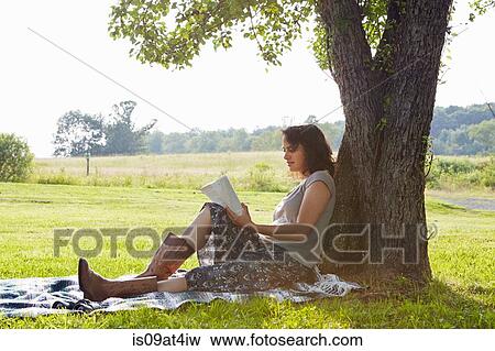 Woman reading book whilst leaning against tree View Large Photo Image Stock Photo - Woman reading book whilst leaning against tree. Fotosearch