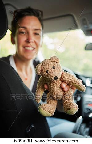 Stock Image - "Woman sitting in car, passing teddy bear through seats". Fotosearch