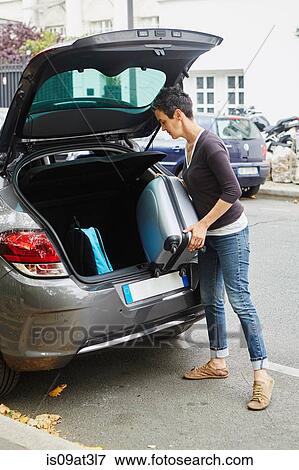 Stock Photo - "Woman standing beside car, putting suitcase in open boot". Fotosearch