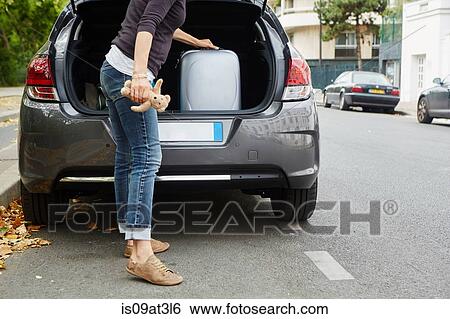 Stock Photograph - "Woman standing beside car, putting suitcase in open boot". Fotosearch