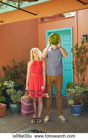 Stock Photograph - Woman with bottle of wine and man covering face with watermelon. Fotosearch