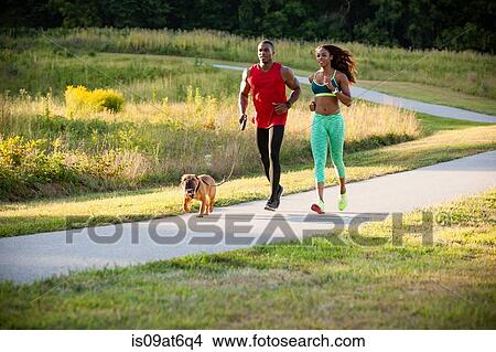 Picture - Young couple and dog running in park. Fotosearch