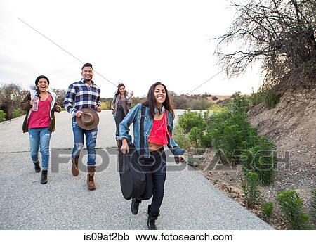 Stock Image - Young man and three adult sisters running along rural road. Fotosearch