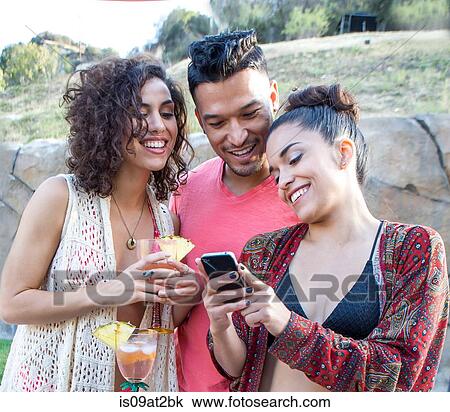 Stock Image - Young man and two sisters reading smartphone texts in garden. Fotosearch