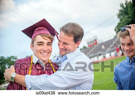Stock Photo - Young man being hugged by father at graduation ceremony. Fotosearch