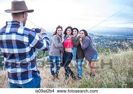 Picture - Young man photographing his four adult sisters on rural hill. Fotosearch
