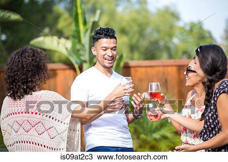 Stock Image - Young man sharing a rose wine toast with adult sisters in garden. Fotosearch