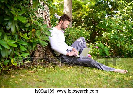 "Young man sitting against tree, using laptop" View Large Photo Image Stock Photo - "Young man sitting against tree, using laptop". Fotosearch