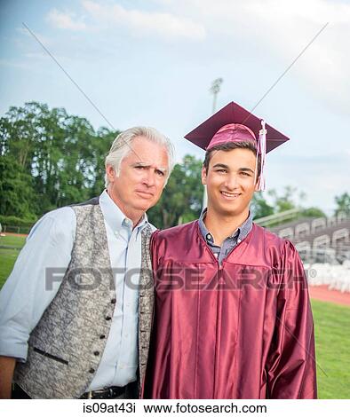 Stock Image - Young man standing with father at graduation ceremony. Fotosearch