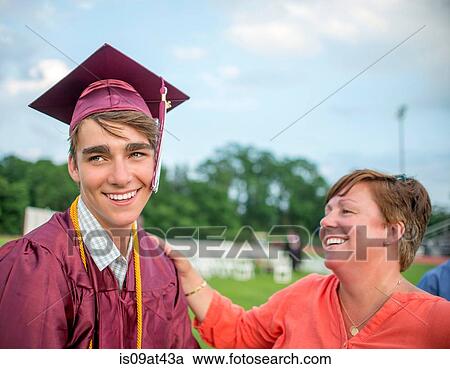 Stock Image - Young man standing with mother at graduation ceremony. Fotosearch