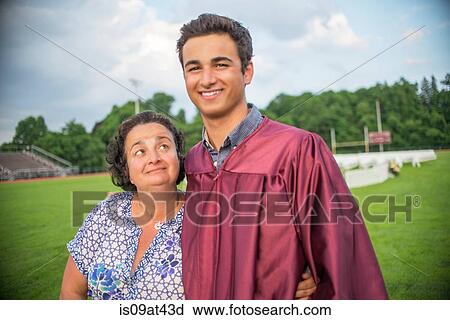 Stock Image - Young man standing with mother at graduation ceremony. Fotosearch