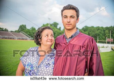 Stock Image - Young man standing with mother at graduation ceremony. Fotosearch