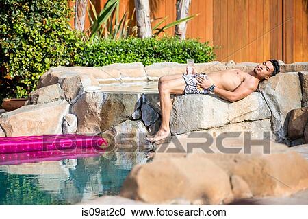 Young man sunbathing on garden swimming pool rocks View Large Photo Image Stock Image - Young man sunbathing on garden swimming pool rocks. Fotosearch
