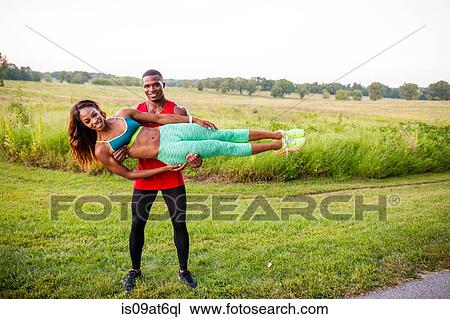 Stock Image - Young man training holding up girlfriend horizontally. Fotosearch